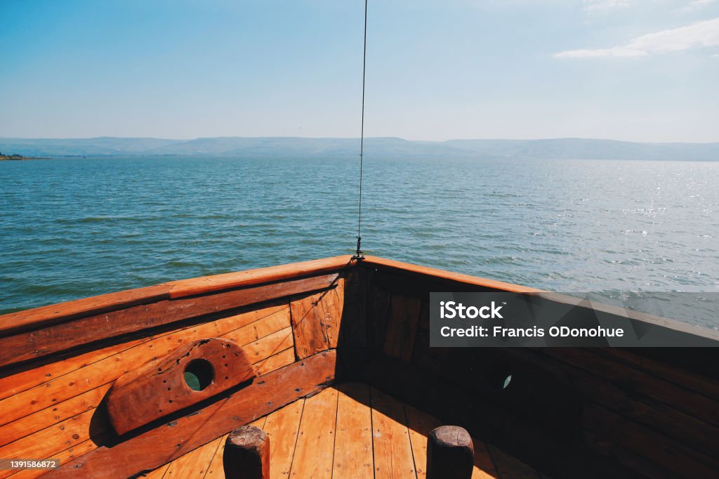 View from the front of a boat sailing the Sea of Galilee A perfect day out on the Sea of Galilee as the rustic Jesus boat takes pilgrims past the towns and locations that Jesus would have frequented. Apostle - Worshipper Stock Photo