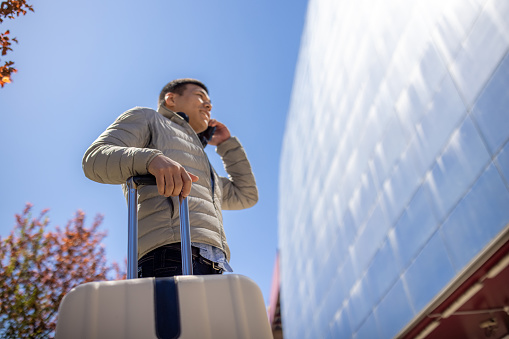 Young man Japanese ethnicity talking on mobile phone while traveling with luggage