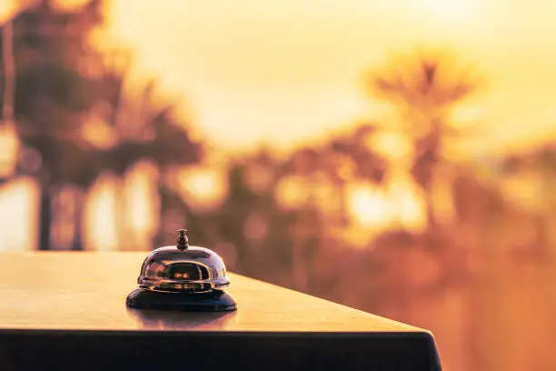 Photo of Beach hotel service bell against the background of coastline sea and palm tree on sunset. Travel concept. 24-hour hotel front desk. Late check-out.