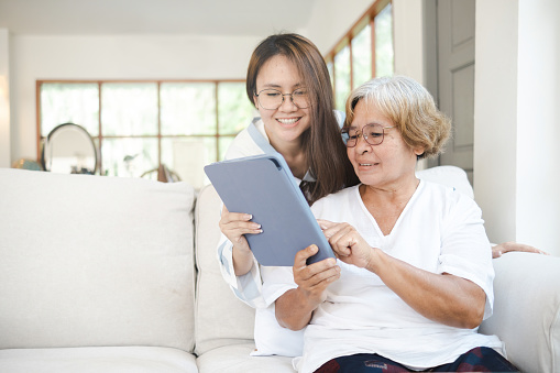Concept love and care for the elderly, an elderly Asian woman looking at the tablet shown by her daughter.