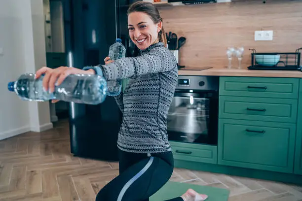 Young woman is exercising at home and using water bottles instead of weights.