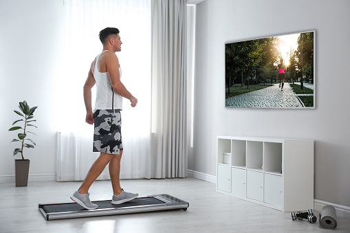Hombre deportivo entrenando en una cinta de correr y viendo la televisión en casa photo