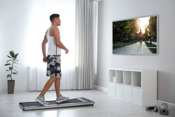 Sporty man training on walking treadmill and watching TV at home Sporty man training on walking treadmill and watching TV at home running shoes on floor stock pictures, royalty-free photos & images