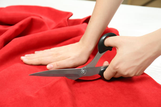 Hand of a young female fashion designer cutting a green fabric for a new suit.