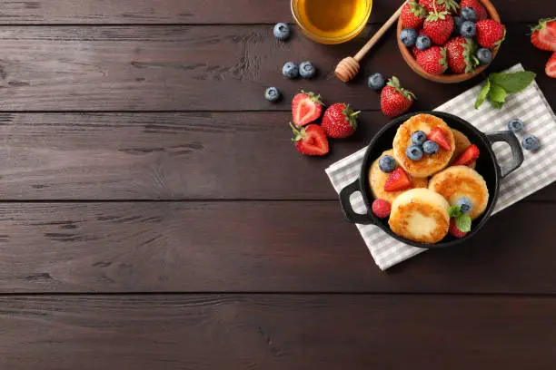 Delicious cottage cheese pancakes with fresh berries and honey on wooden table, flat lay. Space for text