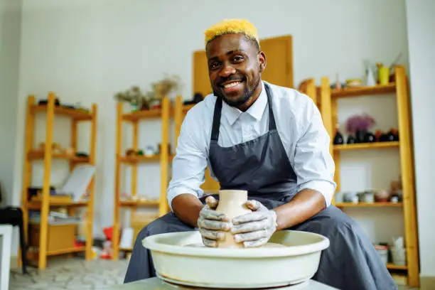 Photo of Portrait of positive latin hispanic brazilian man making ceramic pot on pottery wheel