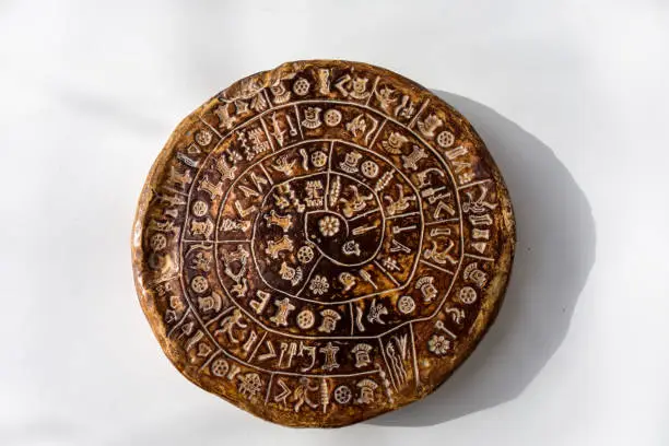 Phaistos disc, Phaestos Disc is an artefact discovered at the minoan site of Phaistos, Crete - Greece. The disk covered on both sides with a spiral of stamped symbols. Isolated on white background.