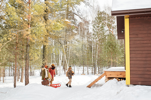 Contemporary black family of three in winterwear moving towards their country house located in the forest to spend weekend there