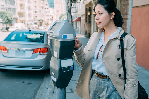 confident asian chinese office lady standing near machine paid parking bill of car. beautiful confident woman worker smiling using card for parking lot. elegant female on street sidewalk in city