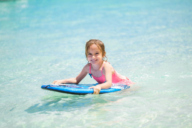 Little baby girl - young surfer with bodyboard has a fun on small ocean waves. Active family lifestyle. Little baby girl - young surfer with bodyboard has a fun on small ocean waves. Active family lifestyle body board stock pictures, royalty-free photos & images