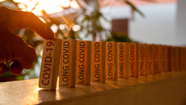 Hand poked on a row of wooden dominoes, with the words "COVID19" and "LONG COVID" stock photo