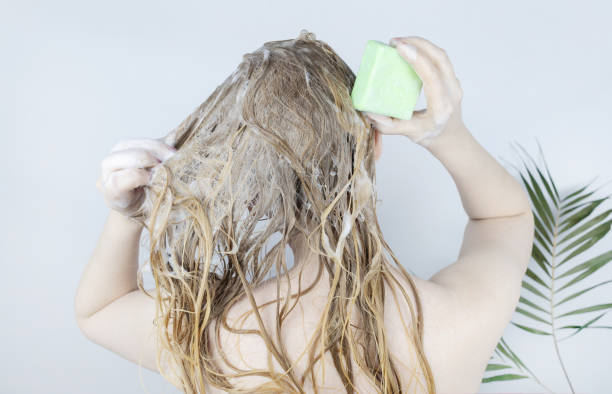 Solid hair shampoo. Close-up of a blonde girl in the bathroom, which lathers her hair with dry shampoo. Lots of foam and peek effect. stock photo