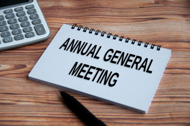 istock Annual general meeting text on notepad with calculator, pen and wooden table background. 1391612936