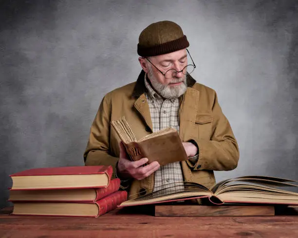 casual studio portrait of a bearded senior man reading and browsing old books