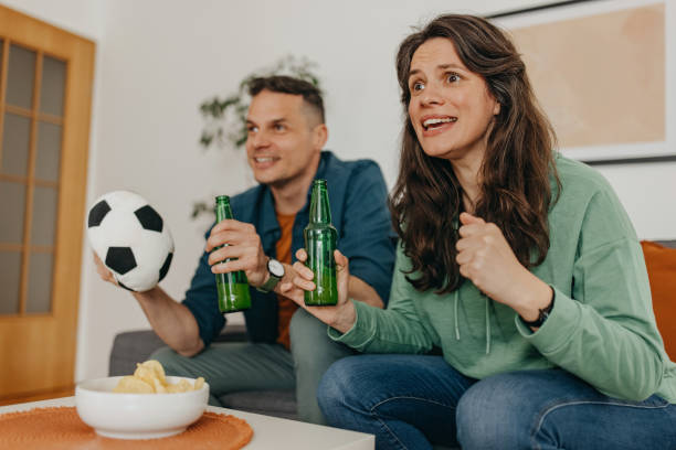 Couple goals Couple sitting on sofa at home cheering while watching soccer match on TV trophy wife stock pictures, royalty-free photos & images