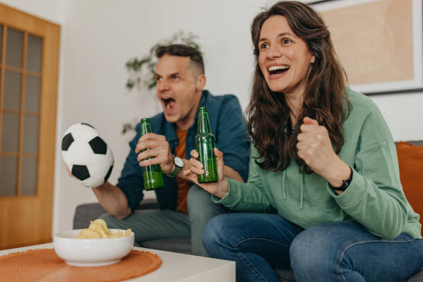 Couple goals Couple sitting on sofa at home cheering while watching soccer match on TV trophy wife stock pictures, royalty-free photos & images