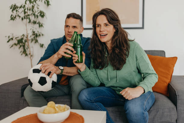 Couple goals Couple sitting on sofa at home cheering while watching soccer match on TV trophy wife stock pictures, royalty-free photos & images