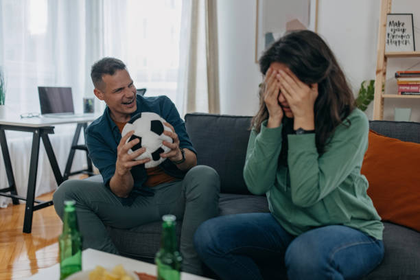 Hope they will win Husband and wife passionately cheering for their different football team at home, woman team loses, she put hands on her face, feeling sad trophy wife stock pictures, royalty-free photos & images
