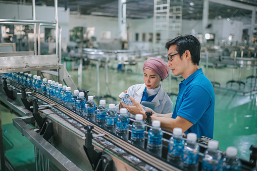 Asian Malay inspector examining quality of mineral water in mineral water factory production line