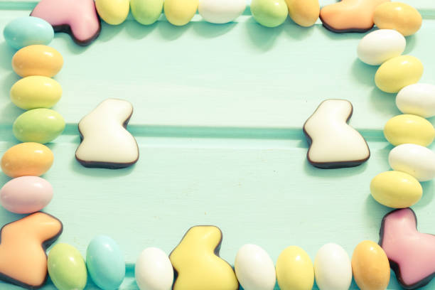 Happy Easter. Pastel color sweet eggs and chocolate rabbits on mint wooden background. Framing. Top view. Copyspace