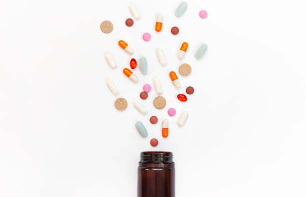 multi-colored pills spill out of a jar on a white background