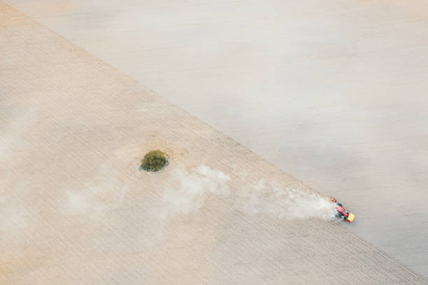 istock Red tractor plowing farm field aerial view looking down from above through clouds. Drone photo cultivation machine equipment working ploughing countryside arable soil driven by farmer spring planting 1391637329