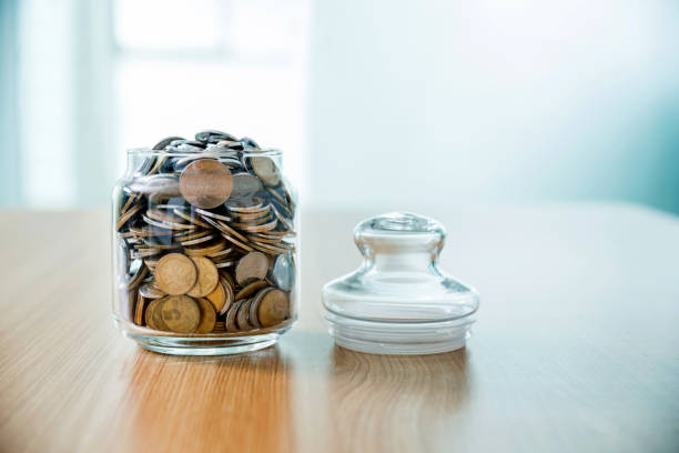 Coins in a jar on wooden table.