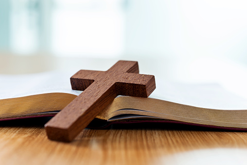 Bible and religious cross on wooden desk.