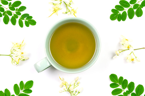 Moringa Tea in ceramic cup with fresh green leaf isolated on white background, top view. Moringa oleifera tropical herb healthy lifestyle concept.