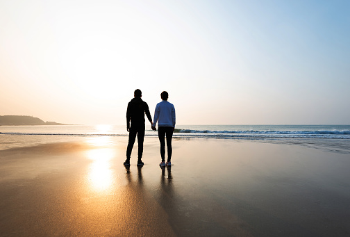 Romantic couple standing on beach at sunset.