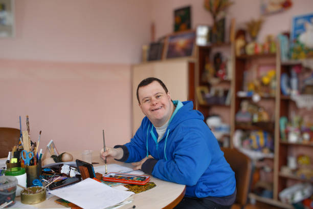 a man with down syndrome is engaged in drawing in a workshop. - downs syndrome work bildbanksfoton och bilder