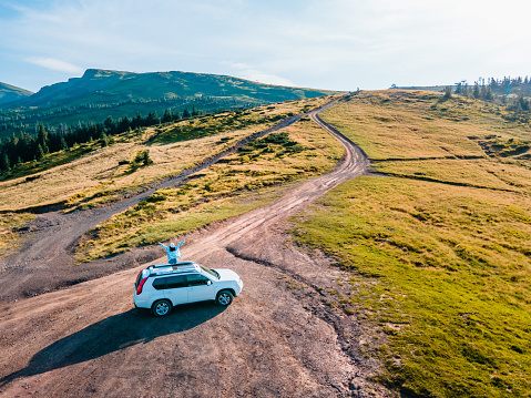aerial view of woman sitting on the roof of suv car enjoying the view. road trip. summertime. Dragobrat carpathian mountains in Ukraine