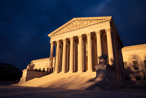 US Supreme Court building in evening sunlight against a dark stormy sky