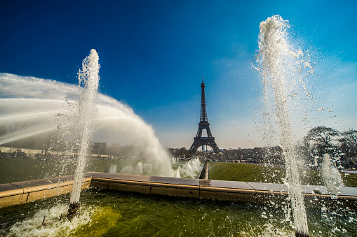 Paris, France - September 4, 2013: Eiffel Tower seen through the water fountains of the Trocadero with Montparnasse in the distance.