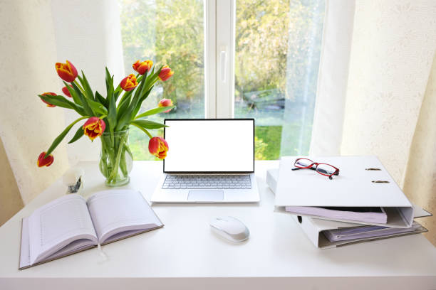 istock Office workplace by the window, laptop with blank white screen, ring binder, organizer and tulip bouquet on a white desk at home, mock up, copy space, selected focus 1391652888