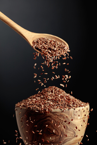 Grains of flaxseed are poured with a wooden spoon in the bowl.