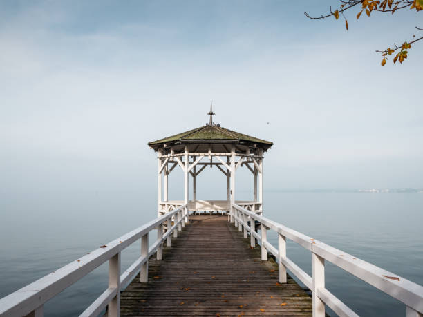 white gazebo on the bank of the lake covered in fog Autumn scene on lake promenade: symmetric photo of white gazebo on the bank of the lake covered in fog bregenz stock pictures, royalty-free photos & images