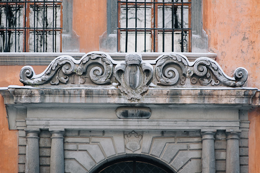 Decorative sculptural reliefs on the facade of a red old building (1580) close-up. Crown symbols, floral patterns, European-style architectural details. Lviv, Ukraine.