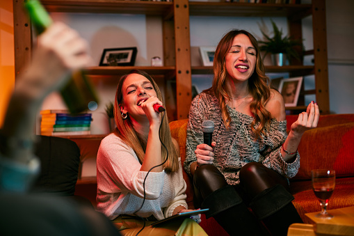 Two beautiful young women are singing karaoke at a home party.