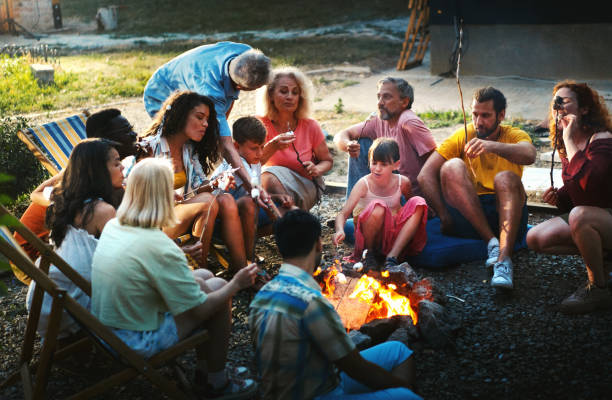 Friends and family spending time by a campfire. Group of mixed age group of people relaxing by a bonfire and cooking marshmallow candy travel9 stock pictures, royalty-free photos & images