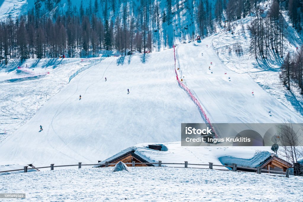 Snow covered house against trees on mountain during winter in alps Snow covered house with skiers in background. Beautiful white landscape covered in snow. Trees on mountains in alpine region during winter. Kronplatz Stock Photo