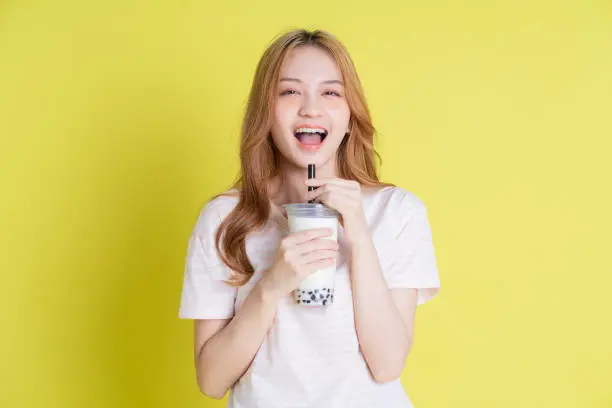 Photo of Image of young Asian girl drinking milk tea on yellow background
