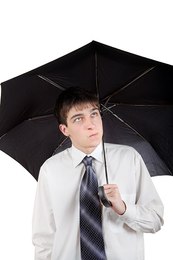 A man in a raincoat walking through a public park during autumn while holding an umbrella. It's rainy and windy.