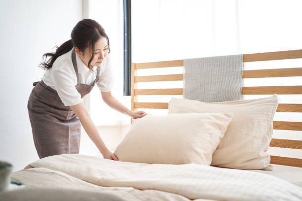 asiatische frau, die ein bett im schlafzimmer macht - dienstmädchen stock-fotos und bilder