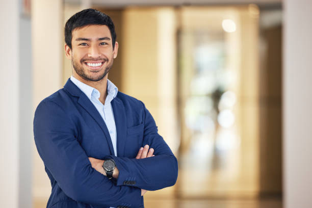 portrait of a confident young businessman standing with his arms crossed in an office - braços cruzados imagens e fotografias de stock