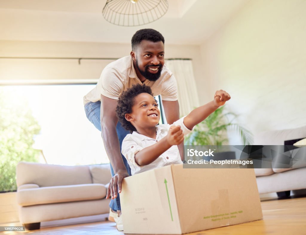 Shot of a father pushing his son in a box while playing together at home Driving his imaginary car, powered by dad Child Stock Photo
