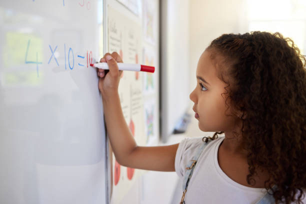 istock Shot of a little girl doing math's on a board in a  classroom 1391720643