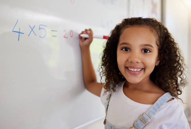 Shot of a little girl doing math's on a board in a  classroom stock photo