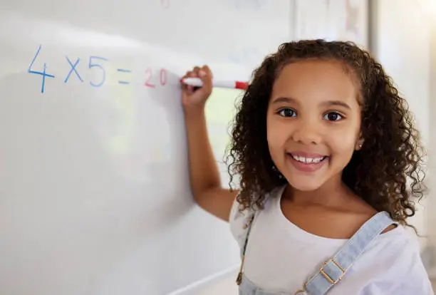 Photo of Shot of a little girl doing math's on a board in a  classroom