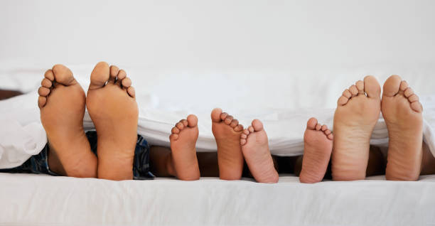 снимок семьи, лежащей босиком на кровати дома - sole of foot стоковые фото и изображения